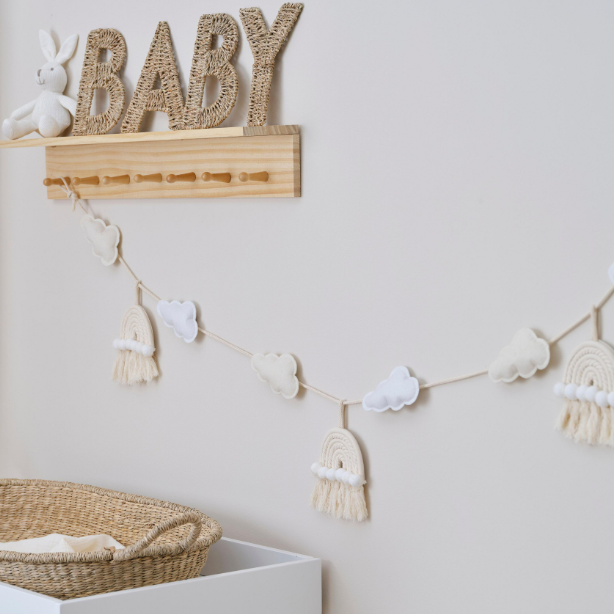 Decorative wall with 'BABY' sign, cloud garland, and woven basket in a neutral setting.