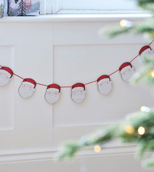 Christmas garland with Santa Claus faces hanging on a wall next to a Christmas tree.