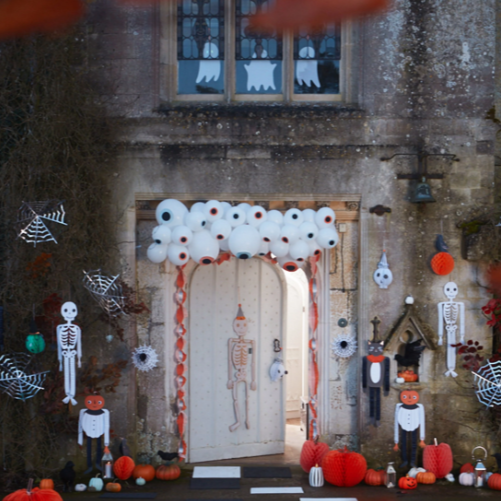Halloween-themed decorations at a house entrance with balloons, pumpkins, and skeletons.