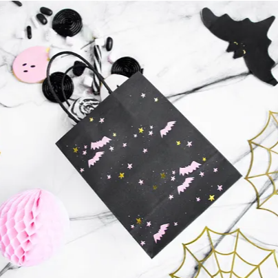 Black Halloween-themed gift bag with pink ghosts and yellow stars on a white surface with decorative elements.