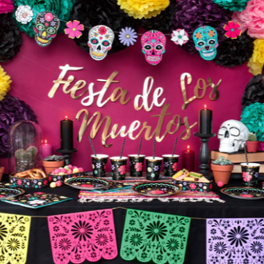 Decorated table for a 'Fiesta de Los Muertos' celebration with colorful skulls, candles, and papel picado.