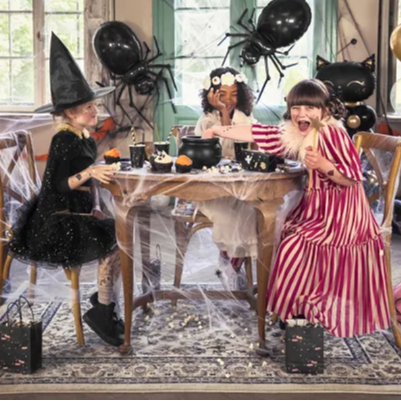 Children in Halloween costumes at a table with spider decorations.