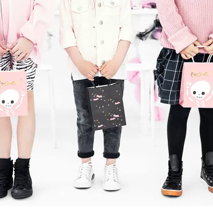 Three children holding pink gift bags with cartoon designs on a white background
