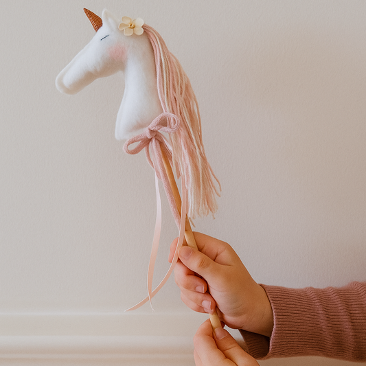 Stuffed unicorn wand with pink hair held by a hand against a plain background
