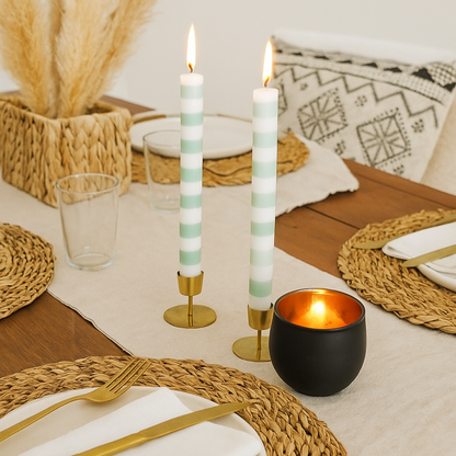 Elegant table setting with candles, gold cutlery, and woven placemats.