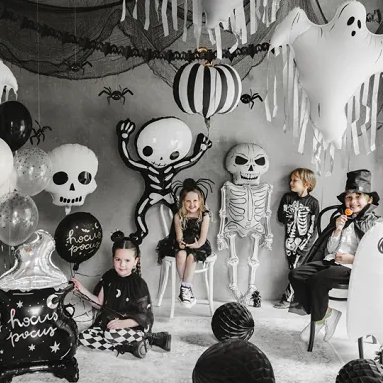 Children in Halloween costumes with decorations including balloons and skeletons in a room.