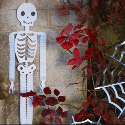 White paper skeleton with red leaves and a spider web on a textured wall.